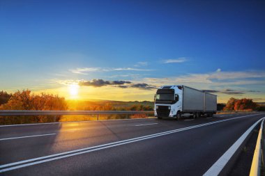 Landscape with a moving truck on the highway at sunset.