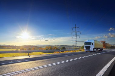 Landscape with a moving truck on the highway at sunset.