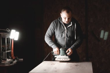 Bir marangoz bir atölyede çalışır. Joiner 'ın öğütücüleri, mobilya üreticileri. Bir marangoz elektrikli zımpara makinesiyle tahta bir parçayı öğütüyor..