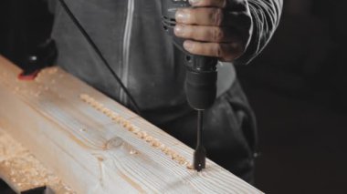 Bir adam atölyesinde matkapla çalışıyor. Bir marangoz karanlık bir odada el gücü ile matkaplar.