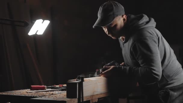 ある男が工房でドリルで作業をしている 指向性光の暗い部屋で手のパワーツールと大工のドリル — ストック動画