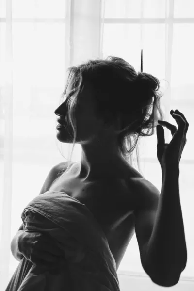 Beyaz çarşafın altına saklanıp ışık penceresinde duran sarışın güzel bir kadının siyah beyaz portresi. Güzel kız pencerede duruyor, battaniyeyle örtülü.