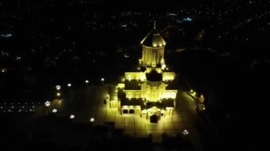 Tiflis 'in Kutsal Üçlü Katedrali' nin etrafında gece aydınlatılmış bir kamera dronu uçuyor.