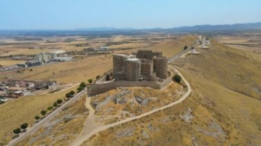 A camera drone flies around over iconic Consuegra Castle (Spanish: Castillo de Consuegra) and windmills