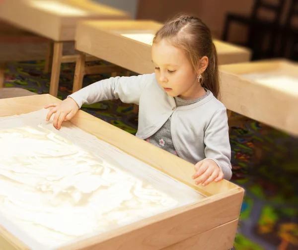 Girl draws with sand on a light table — Stock Photo, Image