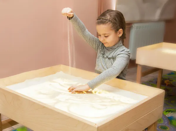 Jenta tegner med sand på et lett bord – stockfoto