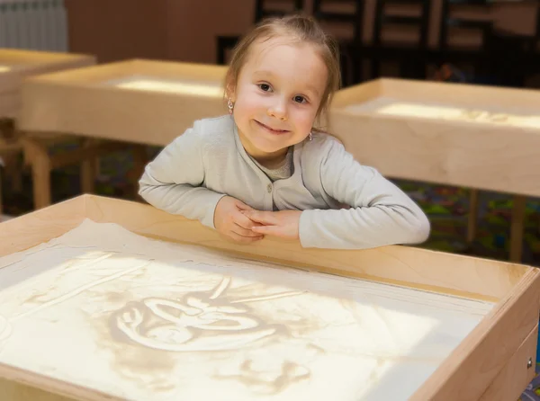 Girl draws with sand on a light table — Stock Photo, Image