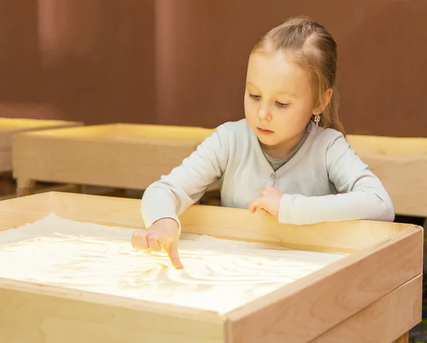 Girl draws with sand on a light table — Stock Photo, Image