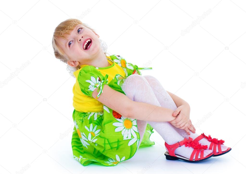 little girl sitting hugging her knees and smiling cheerfully.