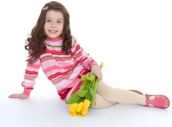 Charmant klein meisje met gele tulpen. — Stockfoto