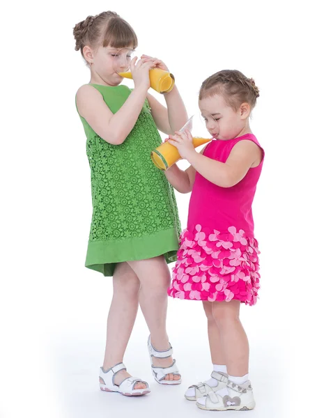 Two little girlfriends drink orange juice. — Stock Photo, Image