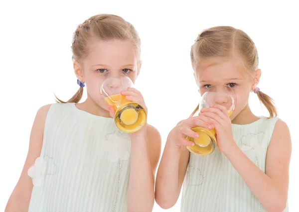 Cute sisters drink from a glass of fresh orange juice. — Stock Photo, Image