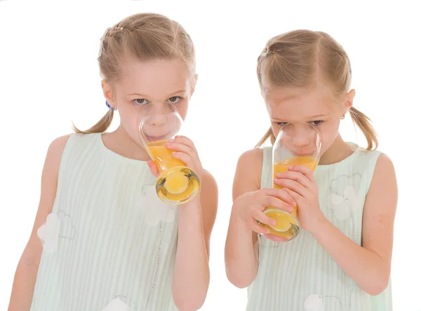 Cute sisters drink from a glass of fresh orange juice. — Stock Photo, Image