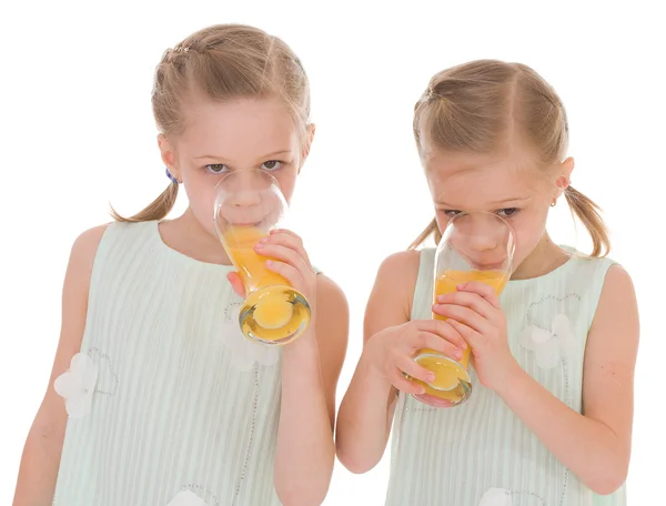 Cute sisters drink from a glass of fresh orange juice. — Stock Photo, Image