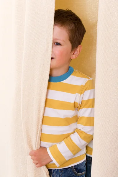 Little boy peeking out from behind the curtains. — Stock Photo, Image