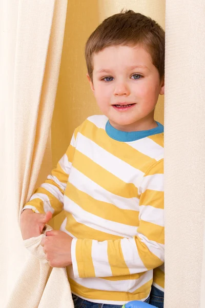 Little boy peeking out from behind the curtains.