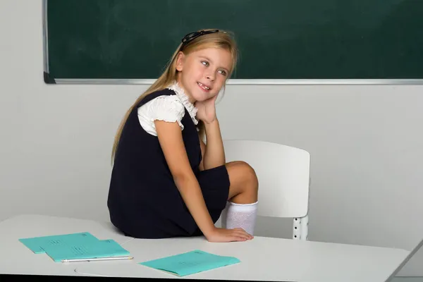 Adorable schoolgirl sitting on desk in classroom — Stock Photo, Image