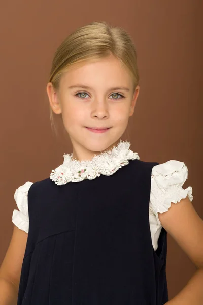 Adorável loira vestindo em blusa branca e vestido azul em pé contra fundo marrom. — Fotografia de Stock