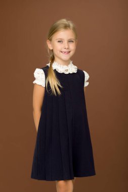 Beyaz bluzlu ve mavi elbiseli sevimli sarışın kahverengi arka planda duruyor..