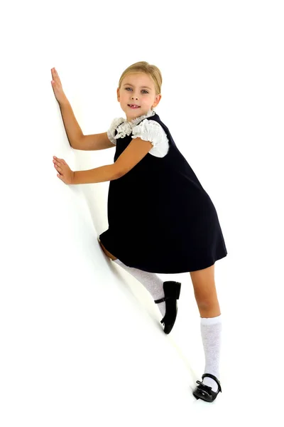 Весела блондинка в білій блузці і блакитна сукня кладе руки на стіну. Прекрасна семирічна дитина стоїть на білому тлі — стокове фото
