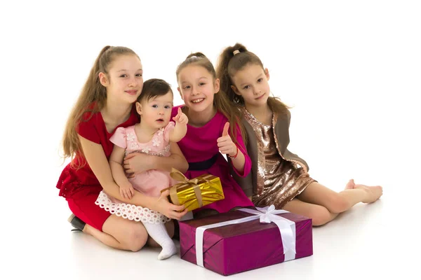 Mädchen unterschiedlichen Alters sitzen auf dem Boden neben Geschenken. Isoliert über weißem Hintergrund. — Stockfoto