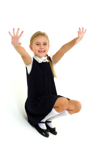 Una rubia alegre con uniforme escolar está sentada en el suelo y agitando las manos —  Fotos de Stock