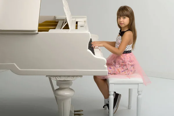 Νεαρή κοπέλα που ποζάρει στο λευκό πιάνο — Φωτογραφία Αρχείου
