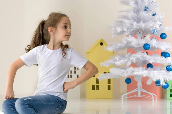 Ragazza in posa accanto all'albero di Natale bianco tenendo Bauble — Foto Stock