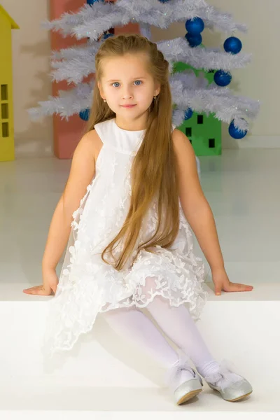 Menina em vestido elegante Sentado no chão na frente da árvore de Natal. Imagem De Stock