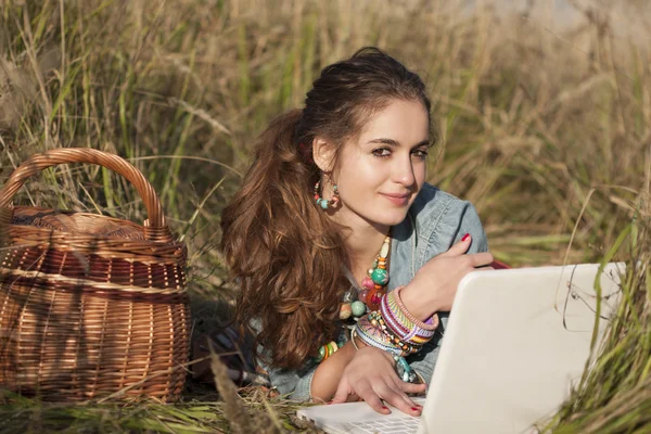 Mujer joven acostada en el campo en el portátil blanco — Foto de Stock