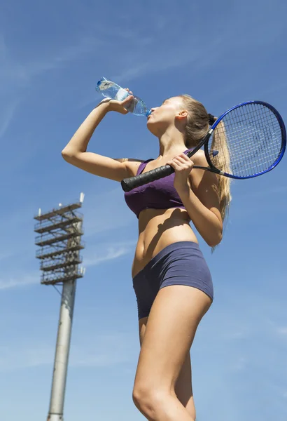 Female tennis player holds racket and drinking water — Stock Photo, Image