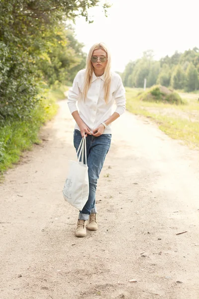 Una mujer camina por el camino con una bolsa en la mano —  Fotos de Stock