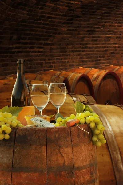 Wine cellar with glasses of white wine against wine barrels — Stock Photo, Image