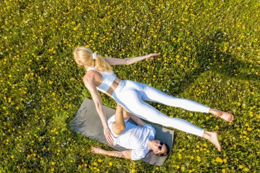 Parkta akro yoga yapan genç ve güzel bir çift. Erkek çimenlerin üzerinde yatar ve kadını ayaklarıyla dengeler..