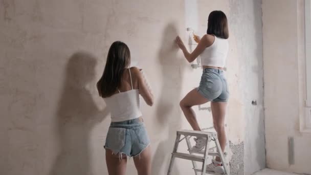 Kaksi naisystävää maalaa seiniä uudessa asunnossa. Happy, nuoret naiset tekevät korjauksia. — kuvapankkivideo