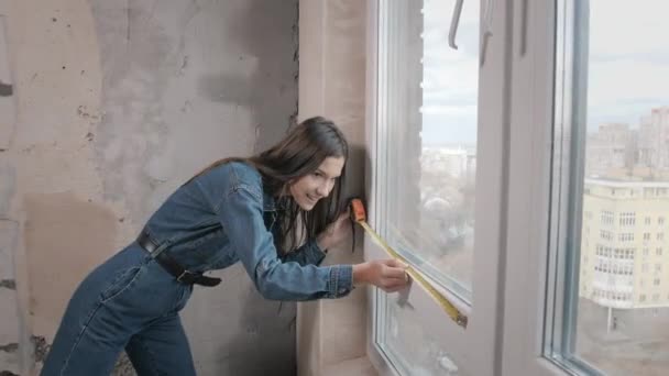 Apartamento de renovación. Una hermosa mujer sonriente hace reparaciones en su apartamento. Paredes vacías, casa de reparaciones con sus propias manos. — Vídeos de Stock