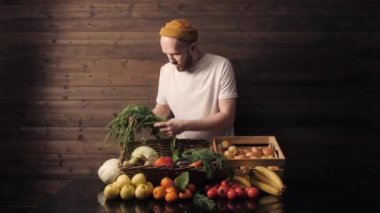 Beyaz tişörtlü ve şapkalı mutlu bir çiftçi bir sepet taze meyve ve sebze tutuyor.