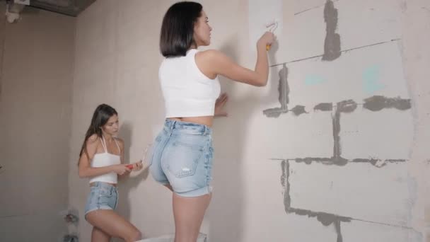 Una mujer feliz hace reparaciones en casa. amigos pintan las paredes en un nuevo apartamento — Vídeo de stock