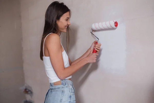 Young beautiful woman makes repairs in the apartment. the girl makes repairs at home on her own paints the walls — Stock Photo, Image