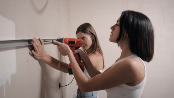 Las mujeres jóvenes hacen reparaciones en el apartamento. Perforación de algo a la pared — Vídeo de stock