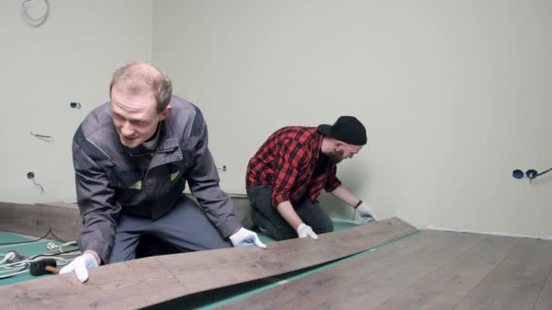 Arbetare lägger laminatgolv i lägenheten. Bostadsrenovering, golvläggning — Stockvideo