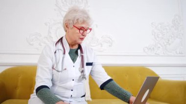 Yaşlı kadın doktor bilgisayarda çalışıyor. Teletıp doktoru bilgisayarla hastayla konuşuyor.