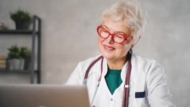 Médico idosa trabalha no computador. Médico de telemedicina conversando com paciente usando laptop — Vídeo de Stock