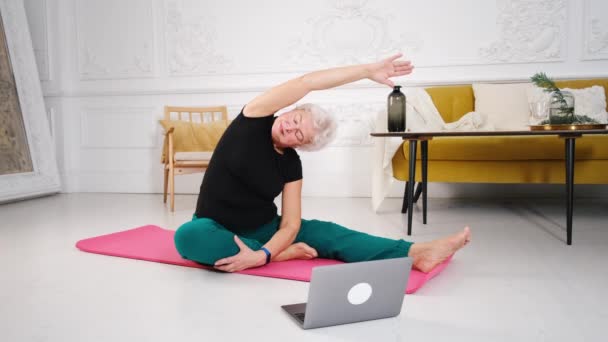Yaşlı bir kadın evde yoga yapıyor. Yaşlılıkta sağlıklı yaşam biçimi kavramı. — Stok video