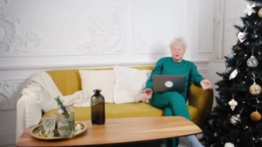 Yaşlı ve güzel bir kadın torunlarıyla video konferans yoluyla konuşuyor. Büyükannenden yeni yıl tebriği