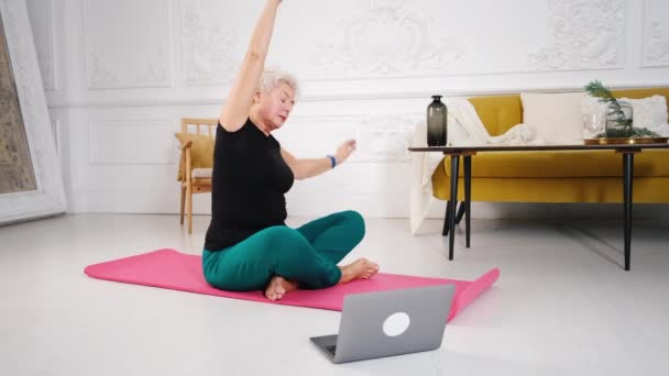 Sportliche Seniorin macht Yoga und schaut Tutorial am Laptop — Stockvideo