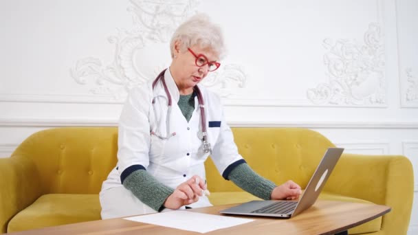 Ärztin mittleren Alters mit Laptop, Notizen mit Stethoskop auf dem Tisch. Gesundheitskonzept. Arzt schreibt und macht Notizen — Stockvideo