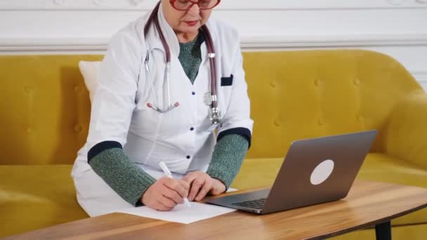Médico femenino de mediana edad usando portátil, escribiendo notas con estetoscopio en la mesa. Concepto de salud. Médico médico escribiendo y tomando notas — Vídeos de Stock