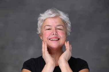 Mutlu 60 'lar orta yaşlı olgun kadın yüz derisine dokunuyor aynada pohpohlanan kameraya bakıyor. Eski sağlıklı kuru cilt bakımı güzellik konsepti, kozmetik ürünleri ve yaş karşıtı estetik cerrahi