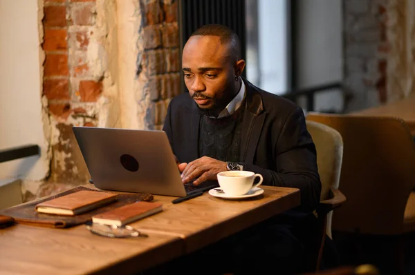 Um afro-americano está a trabalhar num portátil num café. Horário de trabalho gratuito, freelancer — Fotografia de Stock